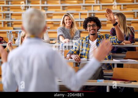 Studente maschile alzando la mano per rispondere alla domanda del professore alla lezione in aula universitaria Foto Stock