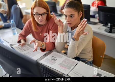 Una studentessa che dà aiuto ad una collega alla conferenza informatica nell'aula informatica universitaria. I giovani intelligenti studiano all'università. Foto Stock