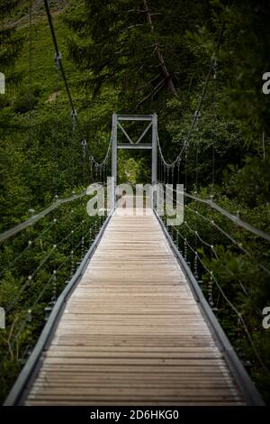 Ponte di legno lungo sopra la gola profonda con una spiaggia di fiume in fondo, tra le rocce. Montagne selvagge nelle Alpi svizzere Foto Stock