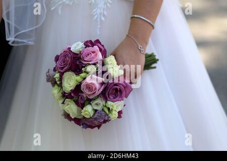 Sposa che tiene un bouquet di nozze in mano contro il sfondo di un abito bianco Foto Stock