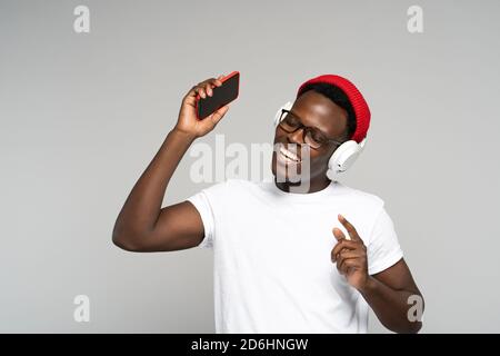 L'uomo afro-americano con le cuffie indossa un cappello rosso, godendosi l'ascolto del nuovo album dell'artista, danze, fa movimenti alla musica, tenendo il phon mobile Foto Stock