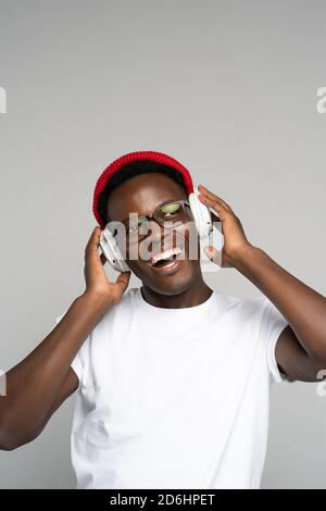 L'uomo afro-americano indossa cappelli rossi e occhiali, godendosi l'ascolto del nuovo album dell'artista, danze, fa movimenti alla musica, tocca hea wireless Foto Stock