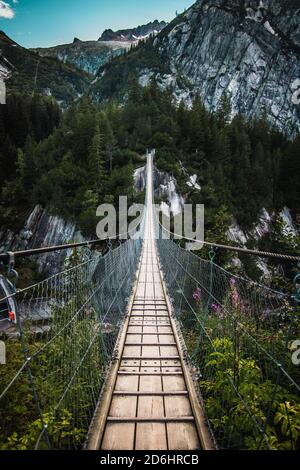 Ponte di legno lungo sopra la gola profonda con una spiaggia di fiume in fondo, tra le rocce. Montagne selvagge nelle Alpi svizzere Foto Stock