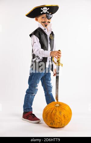 Halloween vacanza. Piccolo ragazzo in costume pirata e con una zucca enorme in lunghezza piena guardando in macchina fotografica su sfondo bianco con spazio laterale vuoto Foto Stock