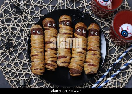 Spooky salsicce mummie e succo di pomodoro per Halloween party su piatto scuro, Flat Lay. Vista dall'alto Foto Stock