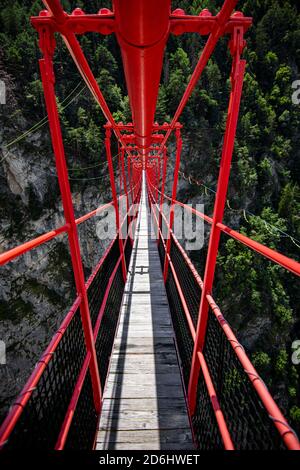 Ponte di legno lungo sopra la gola profonda con una spiaggia di fiume in fondo, tra le rocce. Montagne selvagge nelle Alpi svizzere Foto Stock