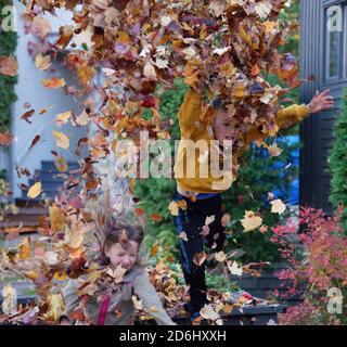 Due bambini, un ragazzo di 8 anni e la sua sorella di 6 anni, saltando e lanciando giocando con foglie d'autunno Foto Stock