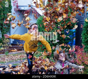 Due bambini, un ragazzo di 8 anni e la sua sorella di 6 anni, saltando e lanciando giocando con foglie d'autunno Foto Stock