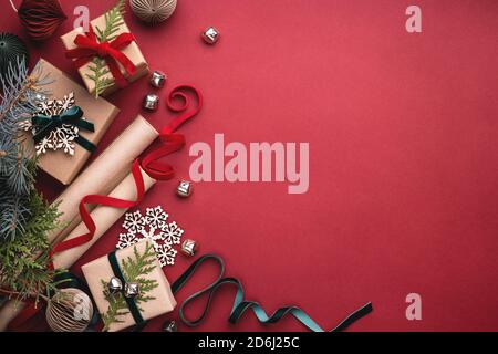 Scatole regalo di Natale, nastri di velluto, rotoli di carta da imballaggio e decorazioni su sfondo rosso. Foto Stock