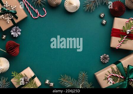 Cornice natalizia con scatole regalo, decorazioni in carta, campane in jingle e rami di abete rosso su sfondo turchese. Sfondo delle vacanze in colori terrosi. Foto Stock