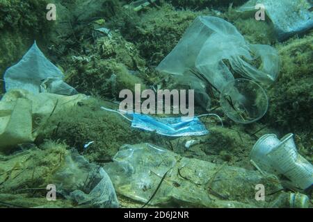 La maschera medica usata scartata insieme ad altri detriti di plastica giace sul fondo marino. Plastica e altri rifiuti inquinanti nel mare Adriatico. Becici Foto Stock