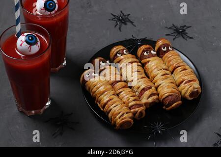 Spooky salsiccia mummie e succo di pomodoro per festa di Halloween su piatto scuro, Closeup Foto Stock