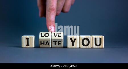 La mano gira i cubi e cambia l'espressione 'ti odio' in 'ti amo'. Splendido sfondo grigio, spazio per la copia. Concetto. Foto Stock