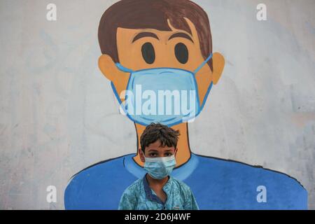 Un bambino palestinese che indossa una maschera facciale vista di fronte a un murale raffigurante un bambino che indossa una maschera su un muro a Khan Yunis, a sud della striscia di Gaza. Foto Stock