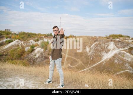 L'uomo elegante con gli occhiali in cape mostra psichico. Uomo adulto con occhiali in posa, in piedi su terreno collinare. Foto Stock