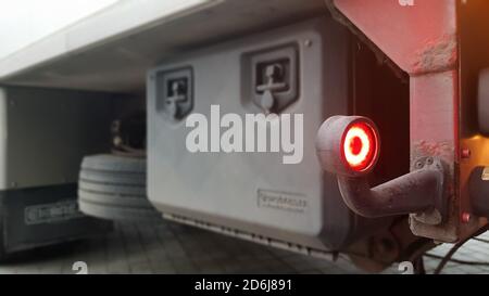 Primo piano della luce d'ingombro rossa rotonda posteriore di un veicolo. Luce posteriore per un carrello. Lo sfondo è sfocato. Il concetto di guida sicura su strada Foto Stock