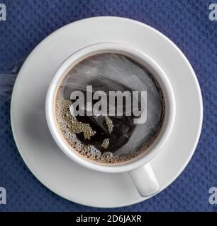 Il caffè fumando in una tazza con il piattino isolato su un sfondo blu che guarda dritto in basso piatto Foto Stock