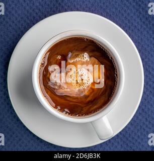 Il caffè fumando in una tazza con il piattino isolato su un sfondo blu che guarda dritto in basso piatto Foto Stock