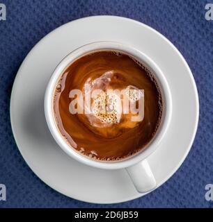 Il caffè fumando in una tazza con il piattino isolato su un sfondo blu che guarda dritto in basso piatto Foto Stock