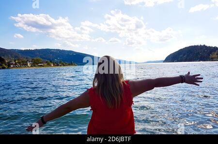 Donna bionda sulla schiena guardando il mare con le braccia alzate in un gesto di gioia Foto Stock