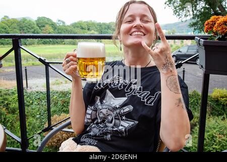 Decin, Repubblica Ceca, 18 agosto 2020: Fan femminile della band Motorhead con birra ceca seduto nel pub-giardino godendosi e sorridendo Foto Stock