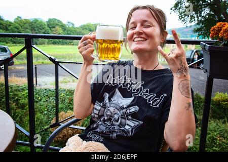 Decin, Repubblica Ceca, 18 agosto 2020: Fan femminile della band Motorhead con birra ceca seduto nel pub-giardino godendosi e sorridendo Foto Stock