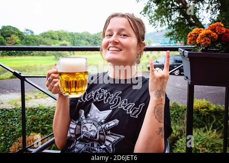 Decin, Repubblica Ceca, 18 agosto 2020: Fan femminile della band Motorhead con birra ceca seduto nel pub-giardino godendosi e sorridendo Foto Stock