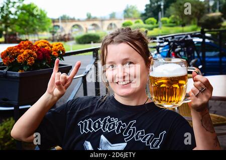 Decin, Repubblica Ceca, 18 agosto 2020: Fan femminile della band Motorhead con birra ceca seduto nel pub-giardino godendosi e sorridendo Foto Stock