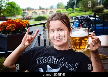 Decin, Repubblica Ceca, 18 agosto 2020: Fan femminile della band Motorhead con birra ceca seduto nel pub-giardino godendosi e sorridendo Foto Stock