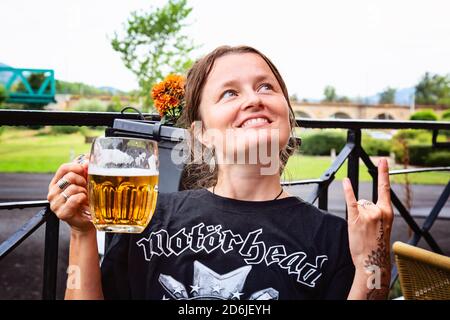 Decin, Repubblica Ceca, 18 agosto 2020: Fan femminile della band Motorhead con birra ceca seduto nel pub-giardino godendosi e sorridendo Foto Stock