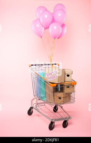 carrello con borse per la spesa e scatole di cartone vicino palloncini sul concetto rosa, nero venerdì Foto Stock