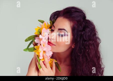 Closeup ritratto giovane latina ispanica donna ragazza che tiene odore toccando una corona di fiori occhi chiusi isolati su sfondo grigio chiaro verde. . Foto Stock