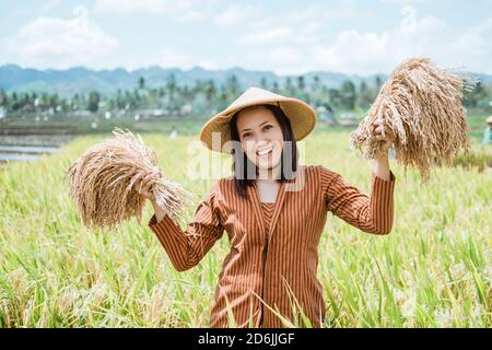 Primo piano di una donna in un cappello in piedi con le sue piante di riso nei suoi campi di riso dopo la raccolta Foto Stock