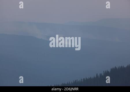 Il fumo denso proveniente dal fuoco del 790 nelle Cascade Mountains blocca gli strati di creste boscose nella luce del tardo pomeriggio. Foto Stock