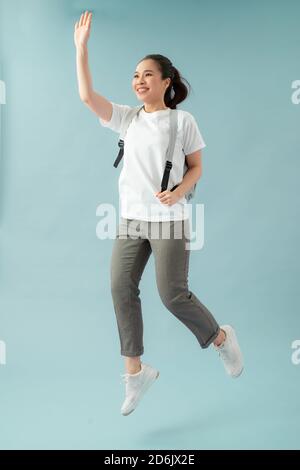 Foto a lunghezza intera di ragazza allegra tenere zaino salto corsa vai lezione salutare i compagni di classe degli insegnanti su sfondo blu Foto Stock