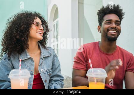 Ritratto di due amici afro che si divertono insieme e si godono del tempo mentre si beve succo di frutta fresca all'aperto presso la caffetteria. Foto Stock