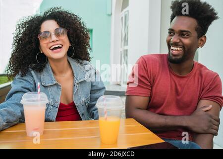 Ritratto di due amici afro che si divertono insieme e si godono del tempo mentre si beve succo di frutta fresca all'aperto presso la caffetteria. Foto Stock