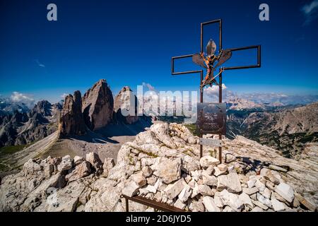 Una croce di metallo sulla cima del Paterno, il monte Paternkofel, il paesaggio delle Dolomiti e il gruppo montuoso tre Cime di Lavaredo in lontananza. Foto Stock