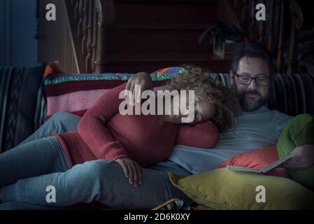 La coppia si rilassa a casa di notte con la donna che dorme e. uomo che legge un libro insieme sul divano - amore e il concetto di vita con le persone sposate che godono il Foto Stock