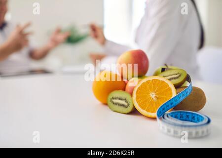 Frutta fresca e nastro di misurazione sulla scrivania contro il dietista offuscato consultazione del paziente Foto Stock