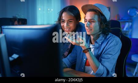 Bella ragazza nera con il suo amico stanno guardando i video sullo schermo del computer e discutendolo. La camera Cosy è illuminata da luce calda e neon. Foto Stock