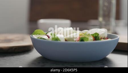 aggiungere la mozzarella alle foglie di insalata mista in una ciotola blu sul piano di cemento, foto ampia Foto Stock