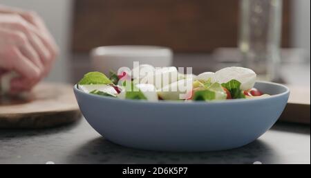 aggiungere la mozzarella alle foglie di insalata mista in una ciotola blu sul piano di cemento, foto ampia Foto Stock