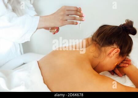 Coltivare la massaggiatrice femmina applicando olio sul retro del cliente mentre preparazione per il massaggio nel centro termale Foto Stock