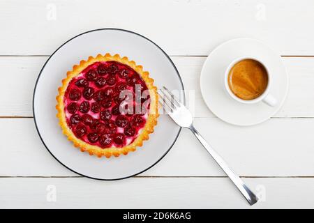 Gustoso tartlet di formaggio di ciliegia fatto in casa e una tazza di caffè espresso su un tavolo di legno bianco. Vista dall'alto. Foto Stock