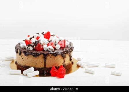 Torta fatta in casa con mousse di banana decorata con ganache, marshmallows e marmellata a forma di bacca su tavolo di legno bianco Foto Stock