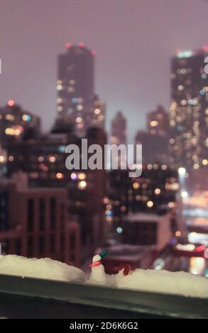 bokeh luci grattacieli città di new york con uomo neve in miniatura sul davanzale whimsical nevoso notte tempo Foto Stock