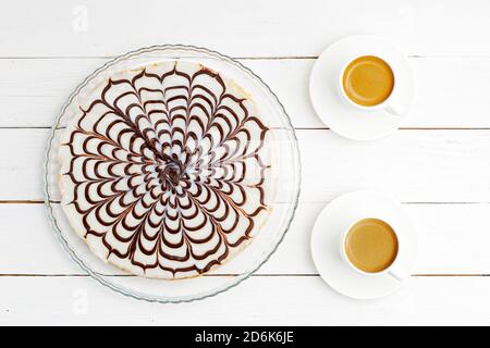 Torta fatta in casa con formaggio casereccio e prugne versate con bianco glassa e due tazze di caffè su tavolo di legno bianco Foto Stock