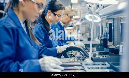 Lavoratori della Female Electronics Factory in Blue Work Coat e occhiali protettivi assemblando schede a circuito stampato per smartphone con pinzette. High Tech Foto Stock