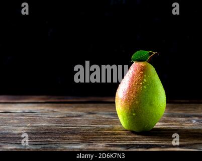 Ancora vita di una pera gustosa con gocce di rugiada e foglia verde. La pera si trova su un vecchio tavolo di legno arancione e su uno sfondo scuro. Tasto foto in stato di scarsa illuminazione. Foto Stock